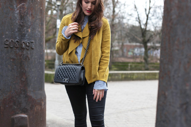 Ein fröhlicher Frühlingslook mit senfgelber Trenchcoatjacke, gestreifter Trompetenbluse und silbernen spitzen Ballerinas